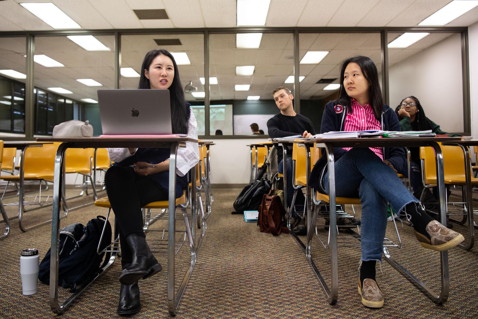 Four students in class with laptops, books, and backpacks.