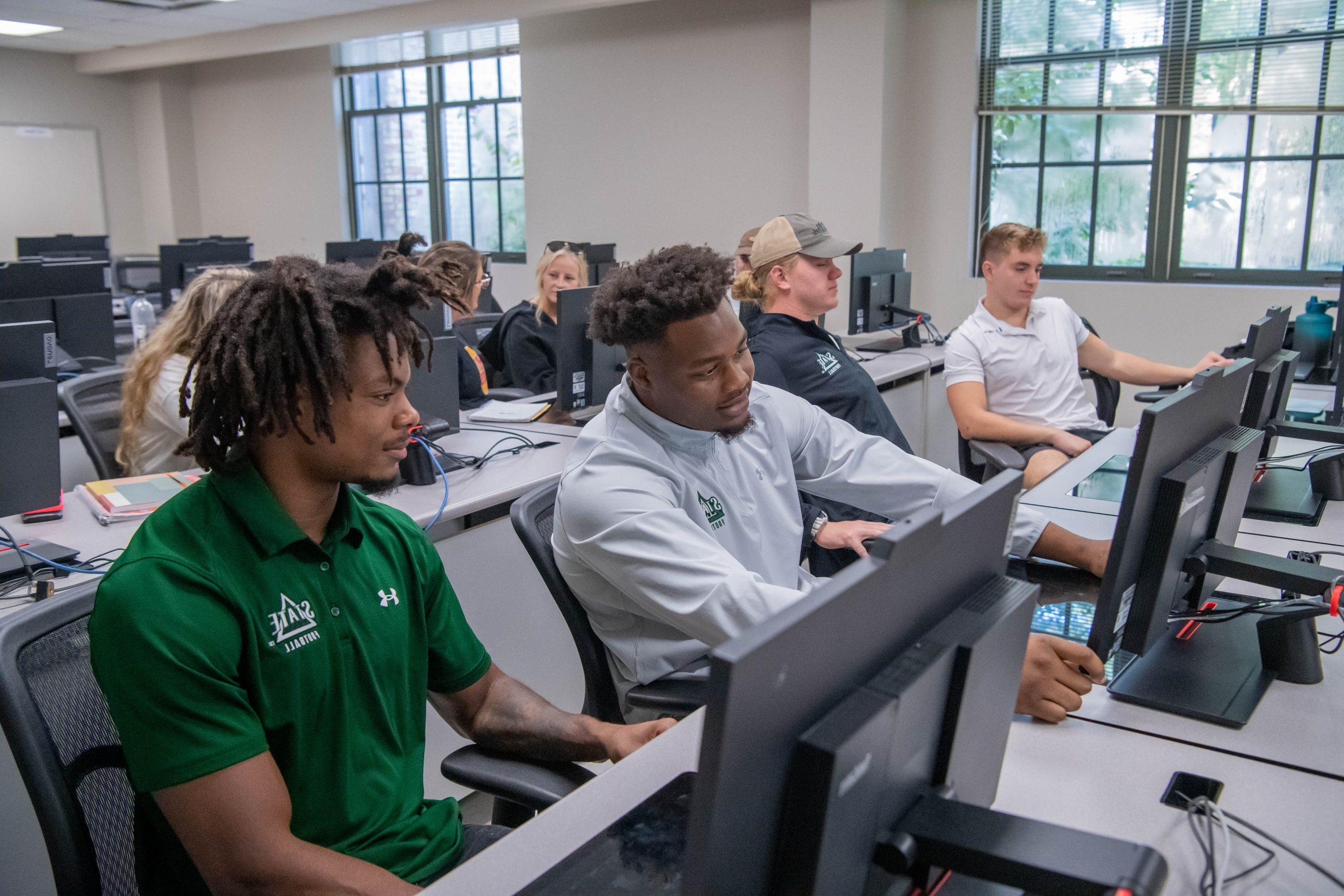 Eight students in a computer lab, working on a assignment together in pairs