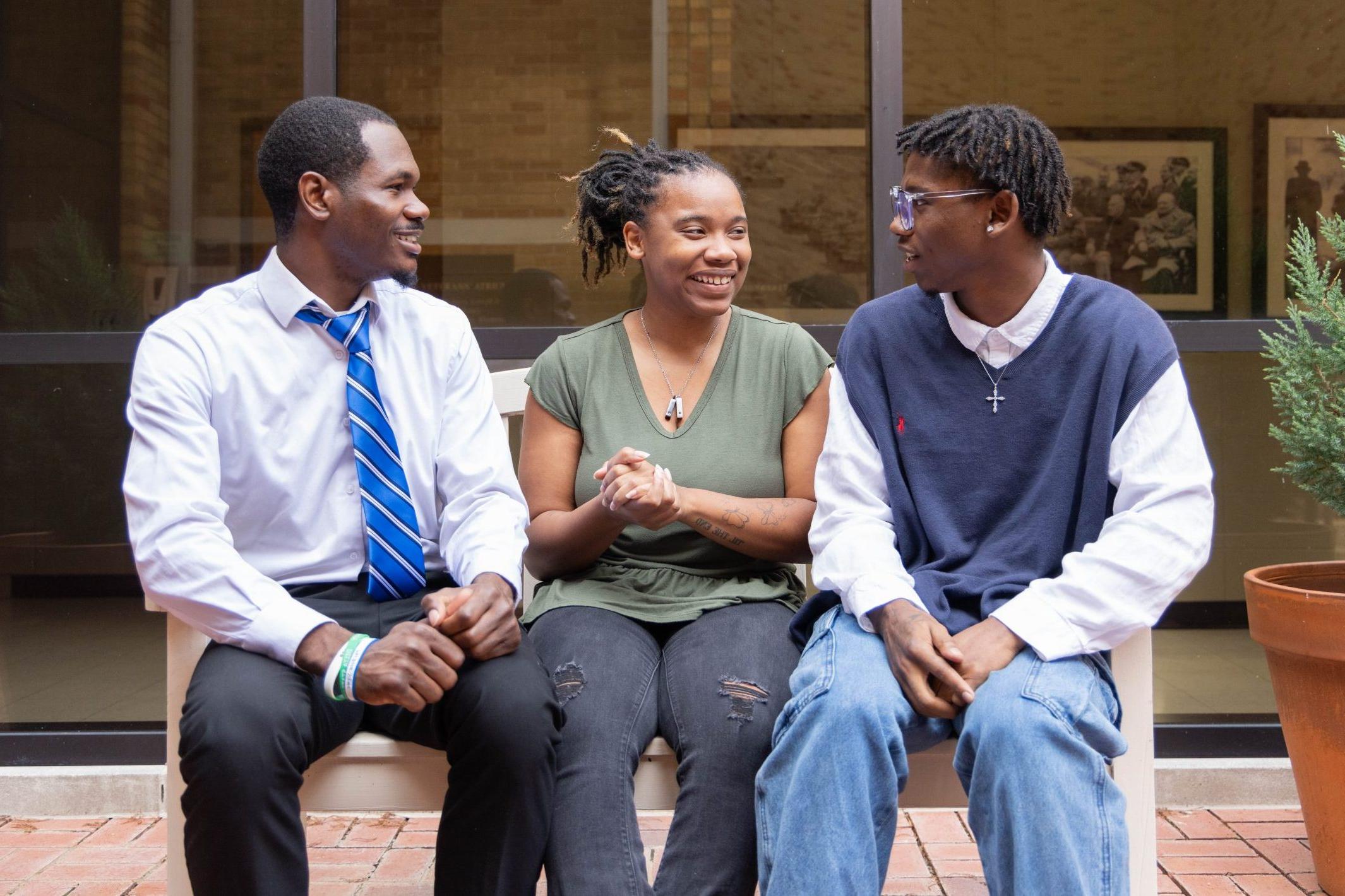 Three African-American students sitting together on a bench outside, engaged in a friendly conversation.